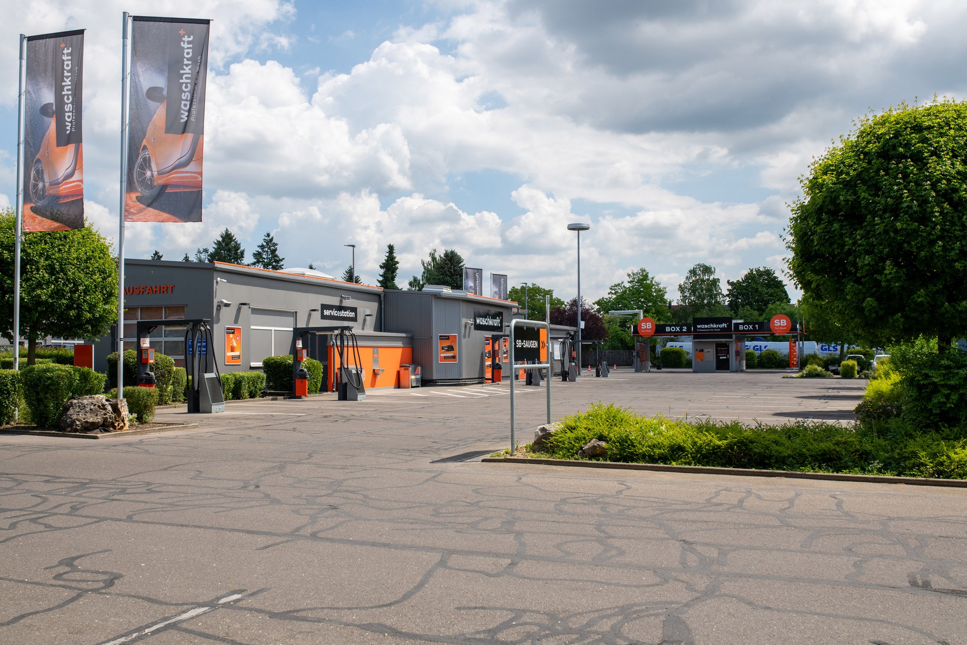 Außenansicht einer modernen waschkraft-Waschanlage mit Fahnen, Parkplätzen und gepflegten Grünflächen an einem sonnigen Tag.